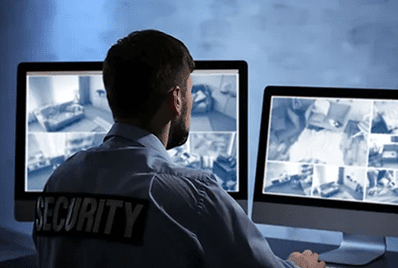 A security guard is looking at two computer monitors.