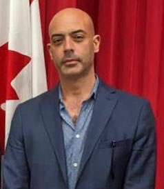 A man in a suit and tie standing next to a canadian flag.